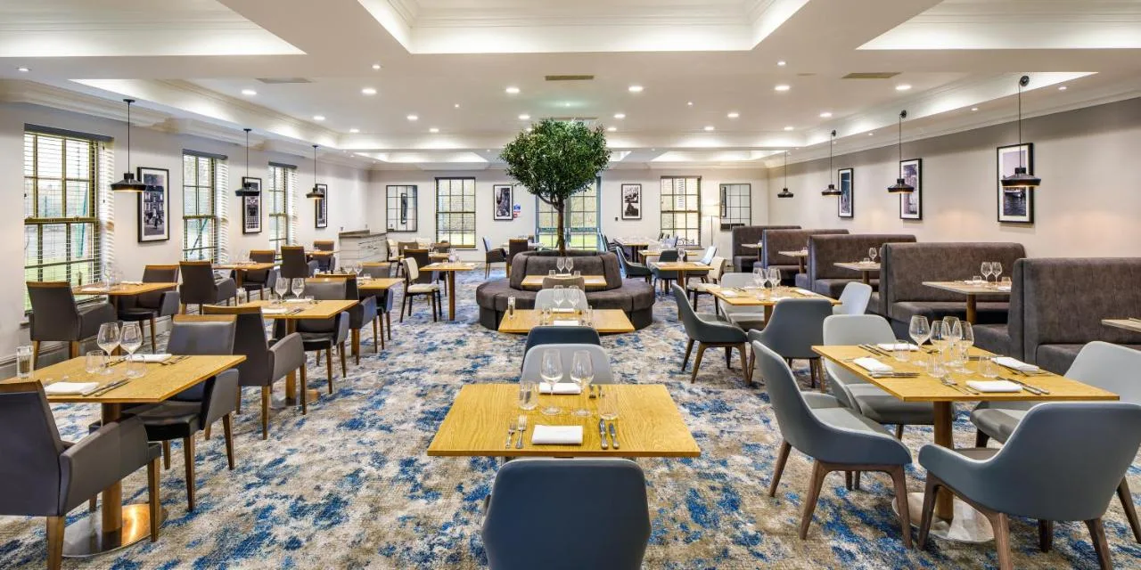 a dining room with tables and chairs and a room with windows at Cambridge Belfry Hotel & Spa in Cambourne