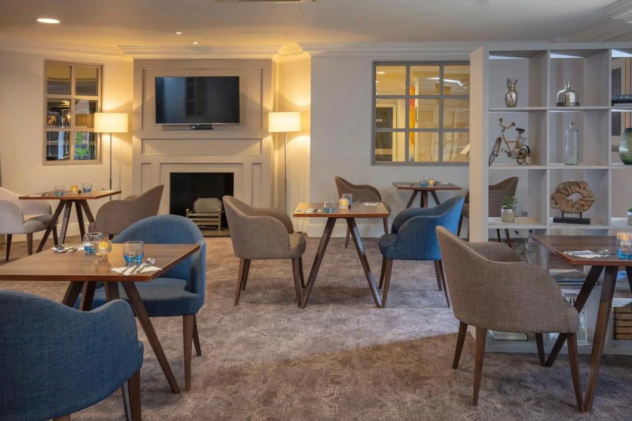 a restaurant with tables and chairs and a fireplace at Cambridge Belfry Hotel & Spa in Cambourne